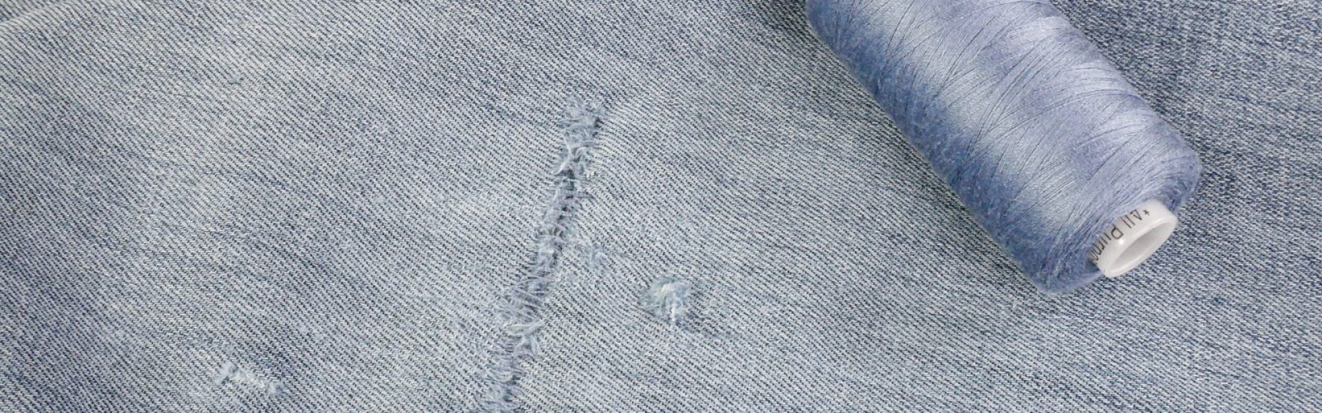 A photo of a torn pair of jeans repaired with hand sewing.